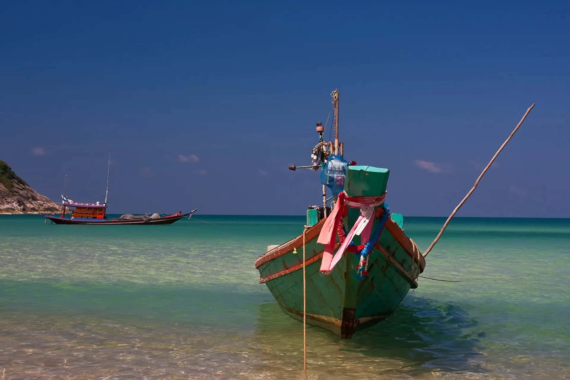 A traditional longtail boat with garlands on its bow, floating in clear water at Bottle Beach