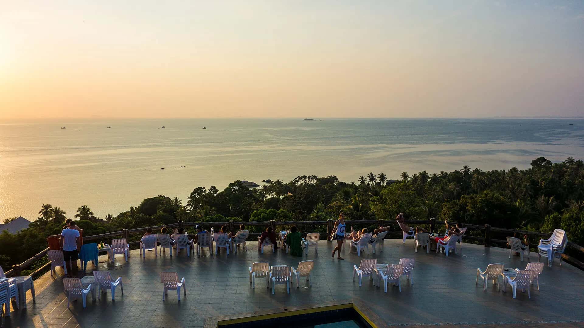 People gathering on a hillside terrace to watch the sun set over the sea