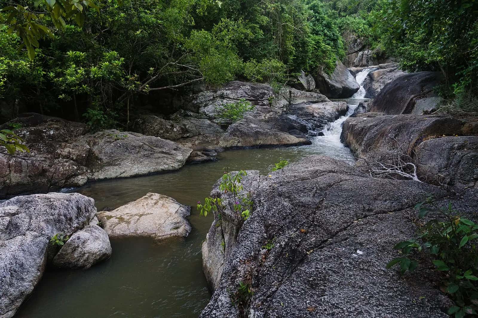 Water cascading between granite boulders into a jungle pool at Than Sadet