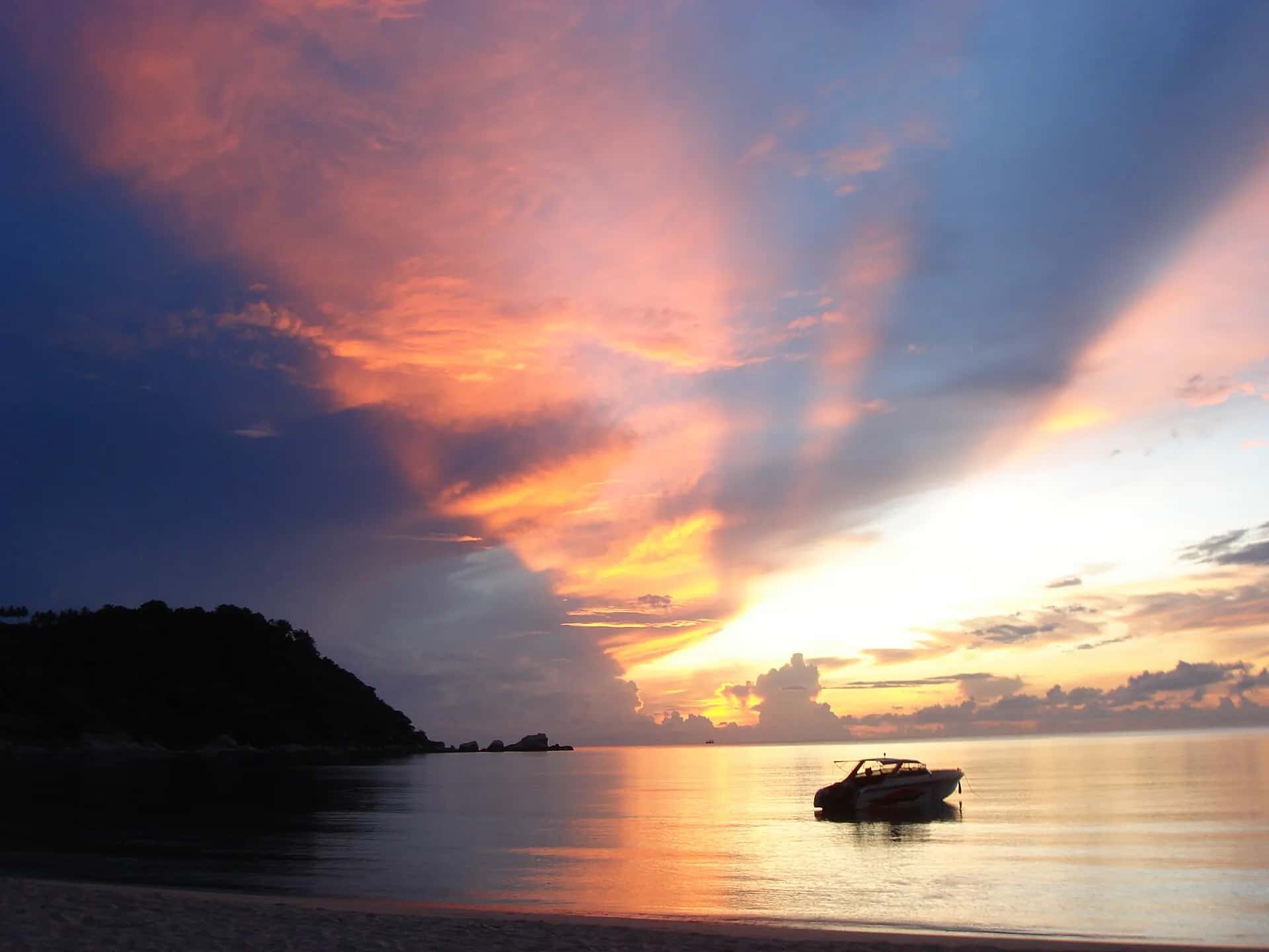 Orange and pink sunrise over Thong Nai Pan bay with a speedboat silhouetted on the water